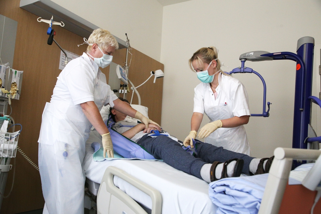 Patient wird mit Hilfe von zwei Pflegerinnen aus Bett gehoben