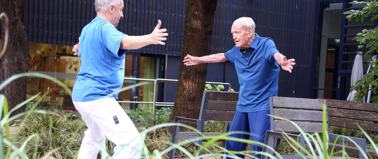 Älterer Bewohner bei Sportübung im Garten mit Pfleger