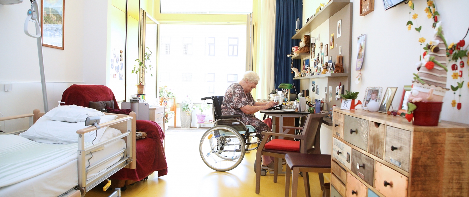 Ältere Bewohnerin im Rollstuhl bei Tätigkeit an ihrem Zimmertisch