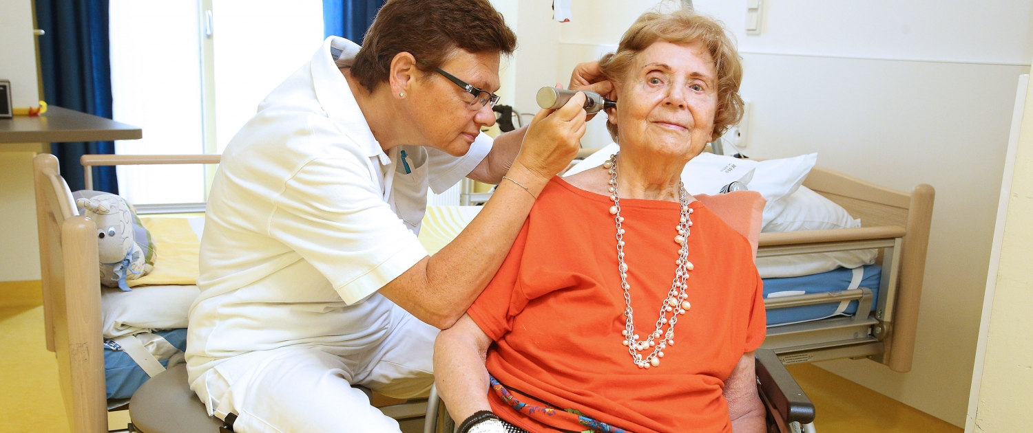 Ältere Patientin wird von Ärztin am Ohr untersucht