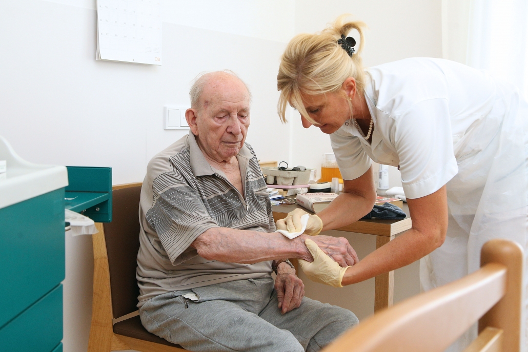 Älterer Bewohner wird von Pflegerin am Arm versorgt